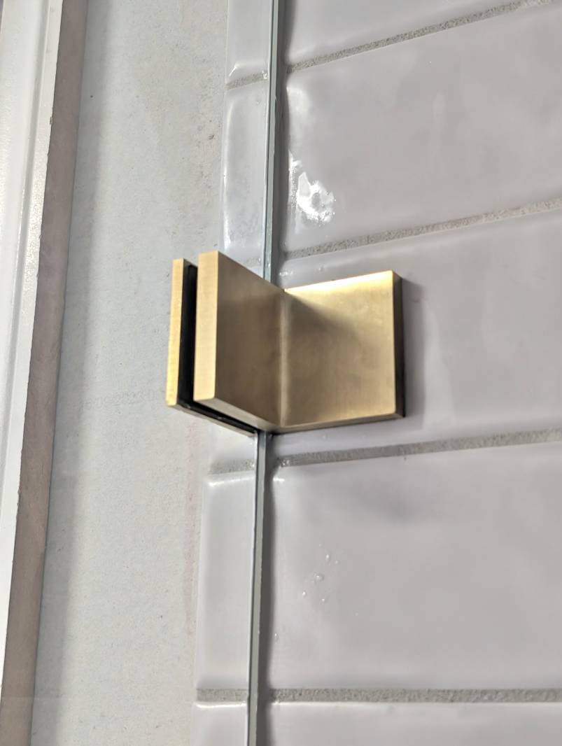 Glass to wall shower screen brackets in brushed gold on white wall tiles