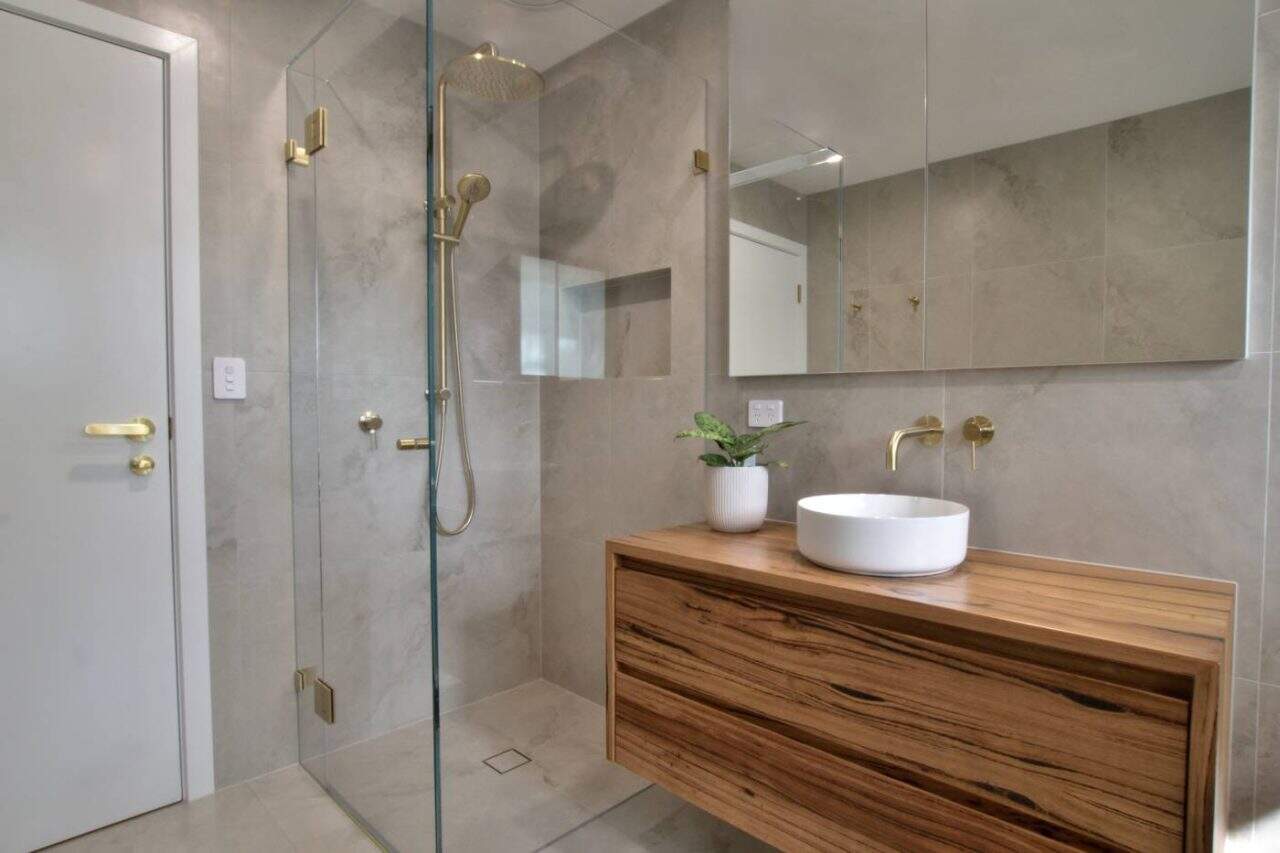 Brushed brass frameless corner shower screen installed in a Melbourne bathroom
