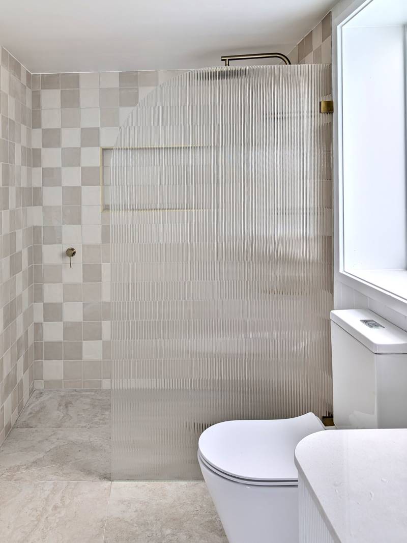 Fluted glass shower panel with radius corner in a walk-in shower with square feature tiles