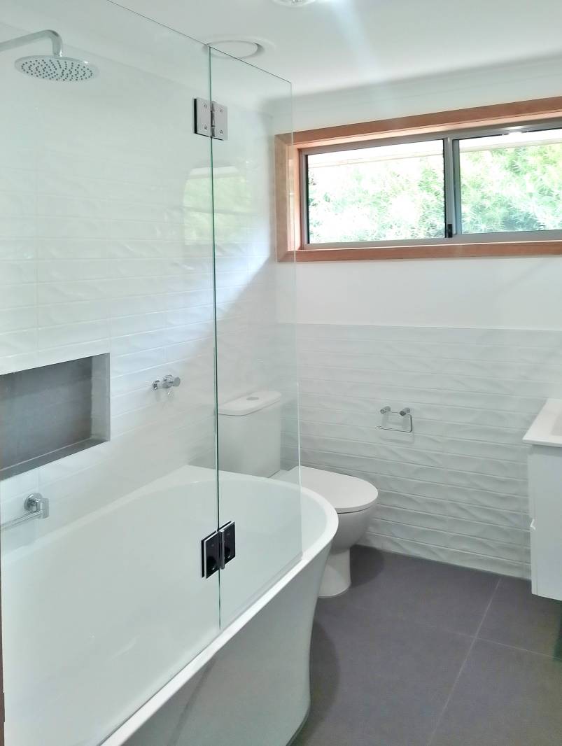 Bathroom with a glass shower screen over bath in a white bathroom with wooden window