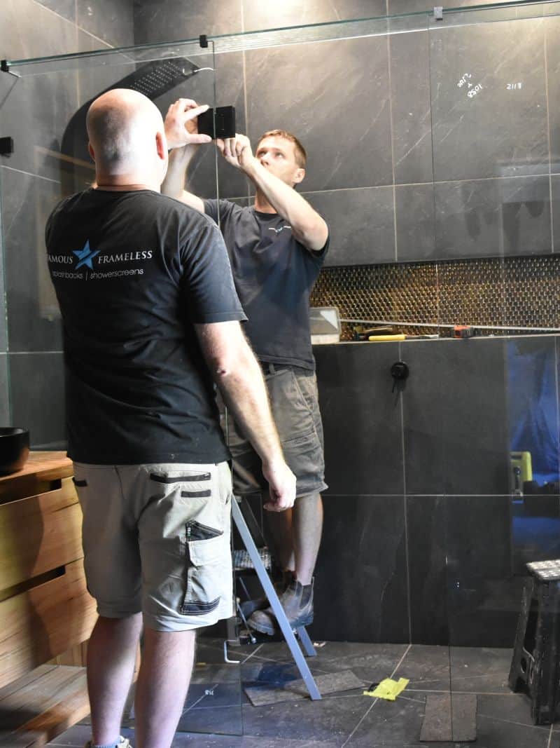 Frameless shower screen installation in Melbourne with black hardware and glass panel being fitted on-site
