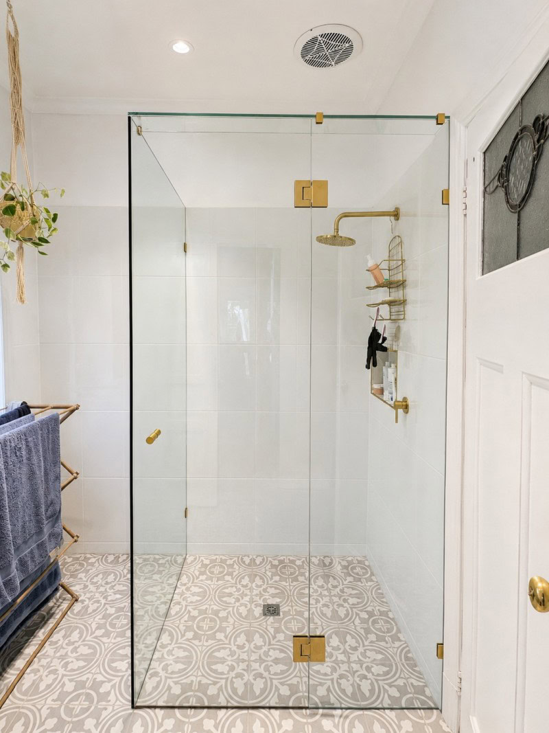 Frameless shower screen with brushed brass hardware in a Coburg bathroom