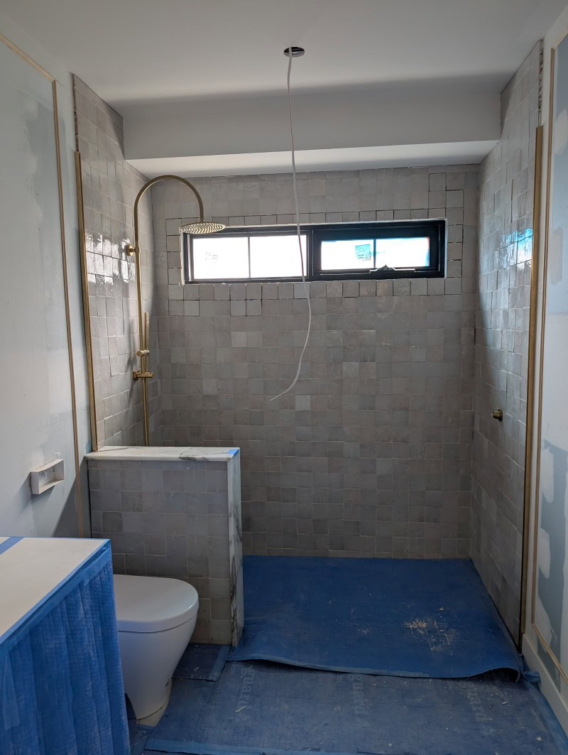 Raw brass wall channels fitted in the back ensuite before glass installation